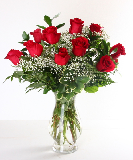 One dozen red roses and greenery in a clear glass vase.