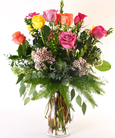 Roses in assorted colors in a glass vase with greenery and baby's breath.